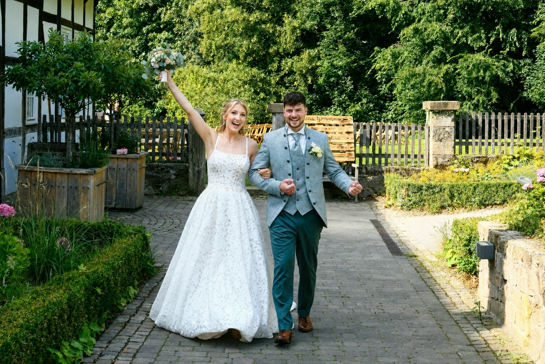 Strahlendes Brautpaar läuft Arm in Arm durch den Hochzeitshof